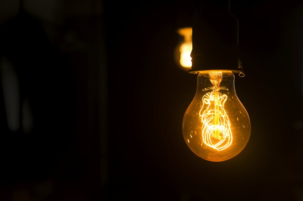 Close-up view of an illuminated vintage light bulb with glowing filament against a dark background.